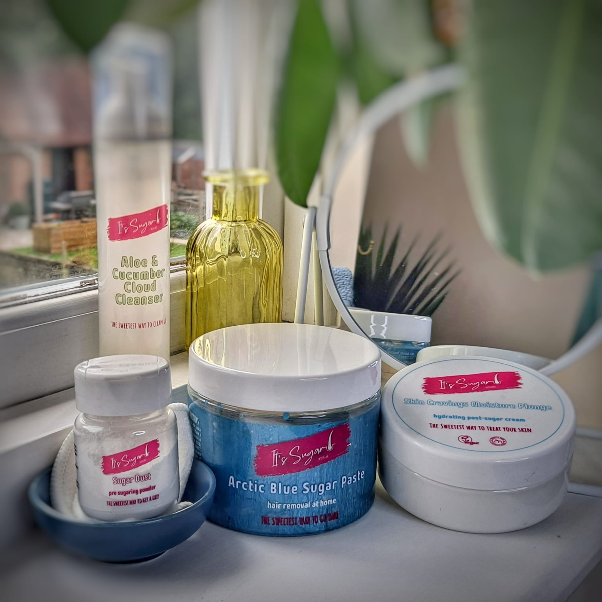 Hair removal kit arranged on white windowsill. 4 products, a small yellow vase, mirror and plant behind them