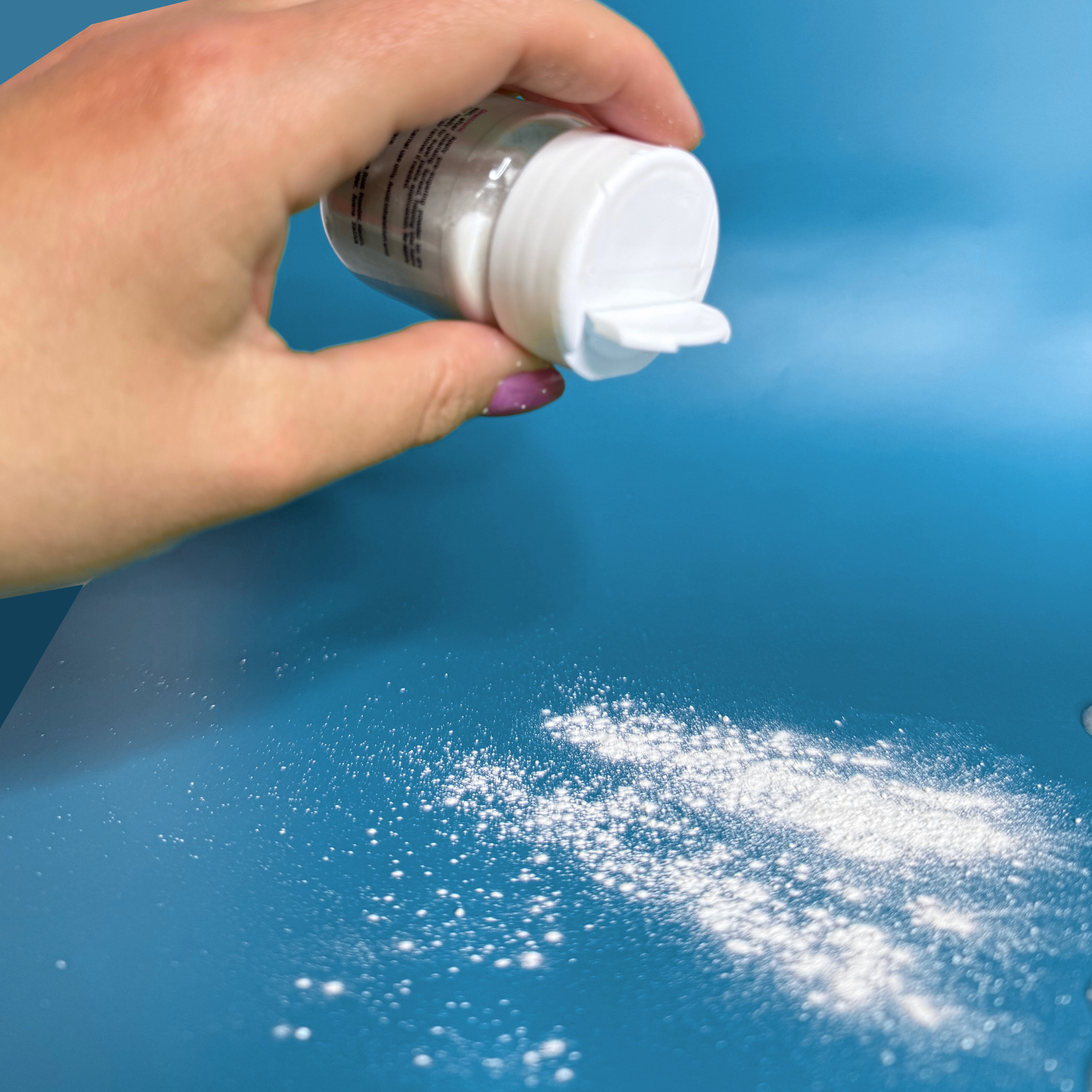 Sugar Dust powder in hand being sprinkled on a blue surface