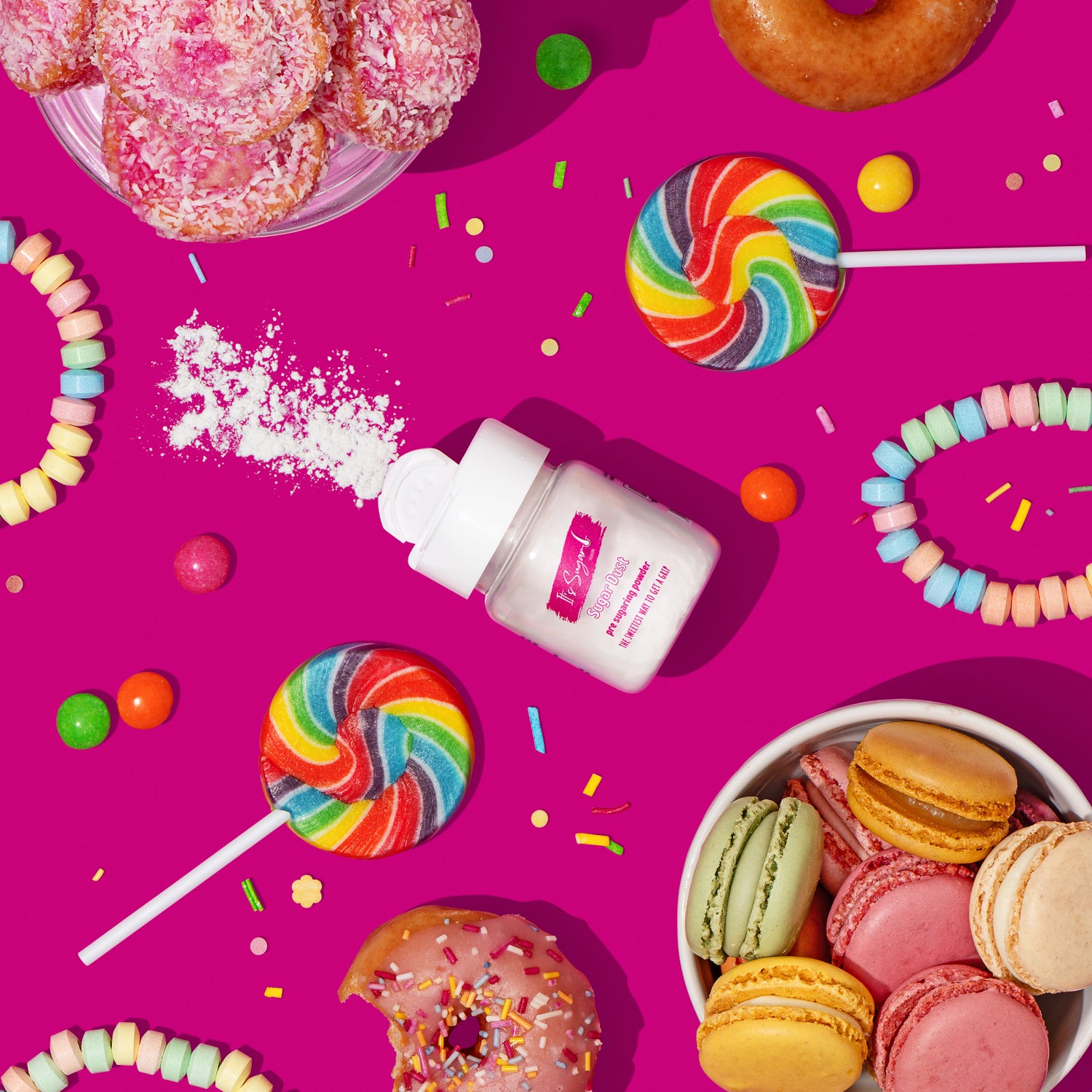 Bottle of Sugar Dust Body Powder surrounded by colourful sweet treats, candies, lollipops, and macarons on a pink background