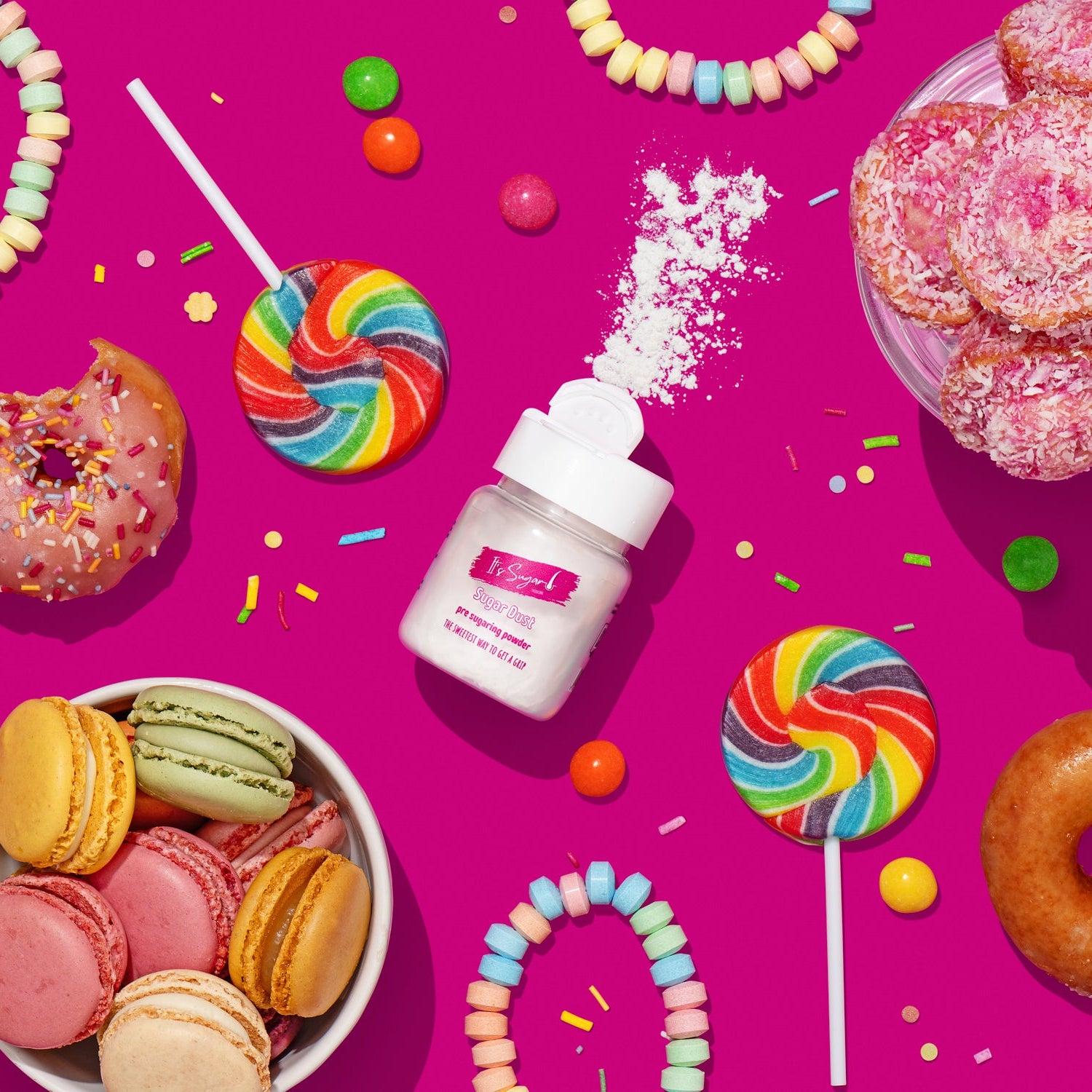 Bottle of Sugar Dust Body Powder surrounded by colourful sweet treats, candies, lollipops, and macarons on a pink background