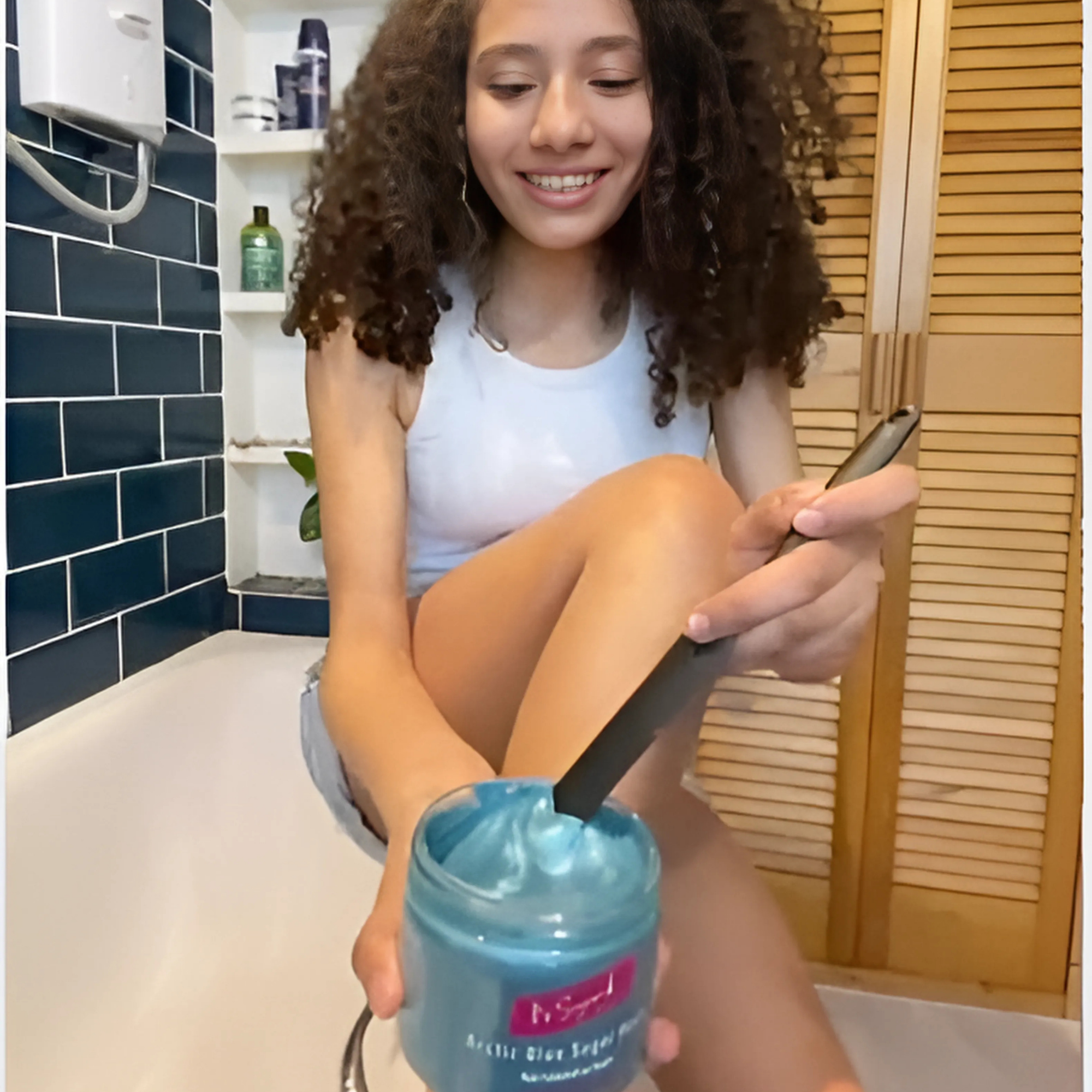 Arctic Blue Sugar Paste by It's Sugar! being stirred with a black applicator by a teen girl, who's smiling, in the bathroom