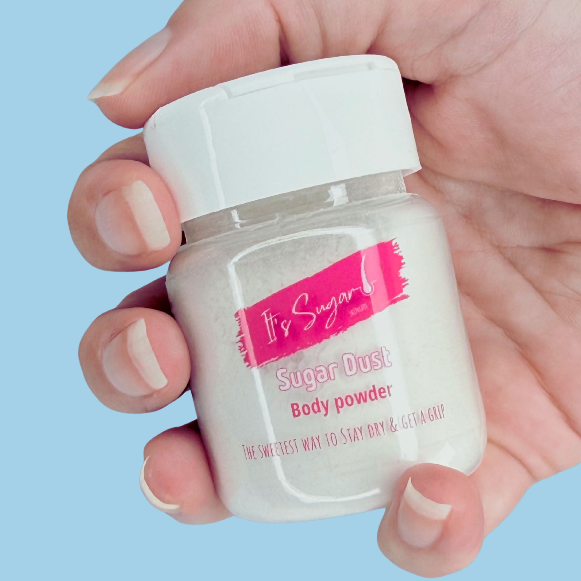 Hand holding a small container of 'It's Sugar' sugar dust body powder against a light blue background