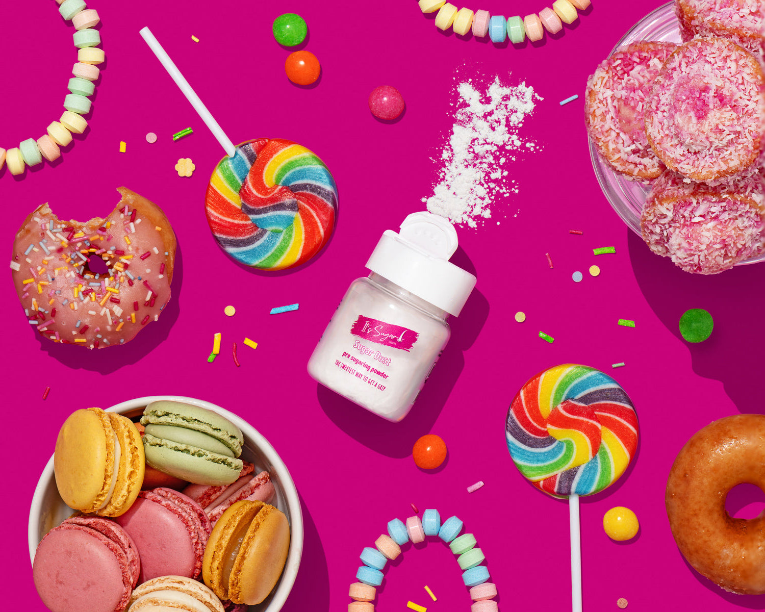 Sugar Dust Body powder in centre sprinkled on bright pink table. Surrounded by colourful sweets, lollies, doughnuts, macrons